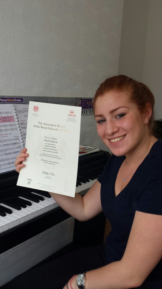 Penguin student Aylin holding her ABRSM Grade 3 piano certificate, passed with merit